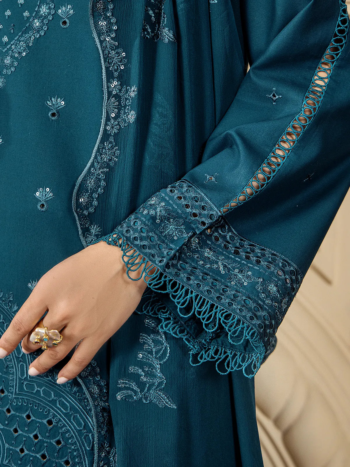 Close-up view of schiffli cutwork lace borders, threadwork sleeves, and loop fringe edging on the teal blue suit by INEJ.