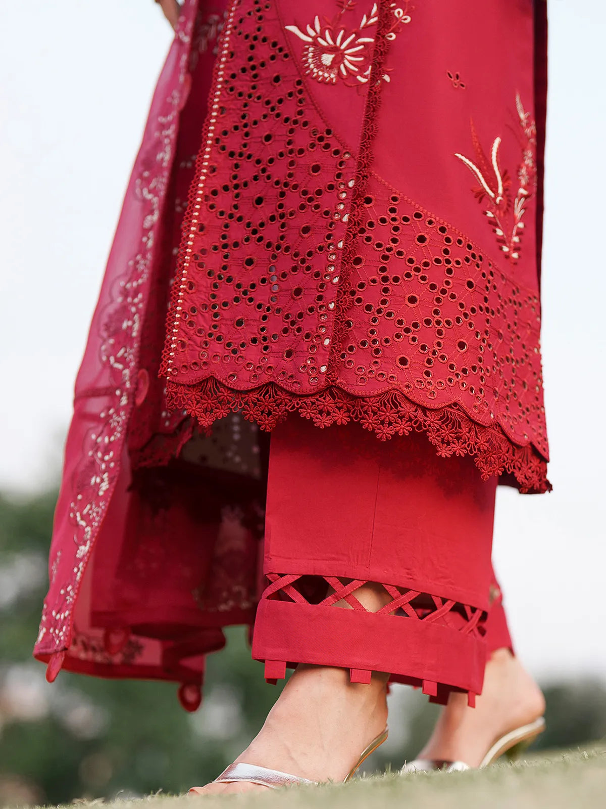 Close-up hem and trouser detail of vibrant red lawn stitched 3-piece suit featuring laser eyelet cutwork daman with scalloped lace edging and criss-cross cutwork trouser cuffs from Baad-e-Saba by INEJ.