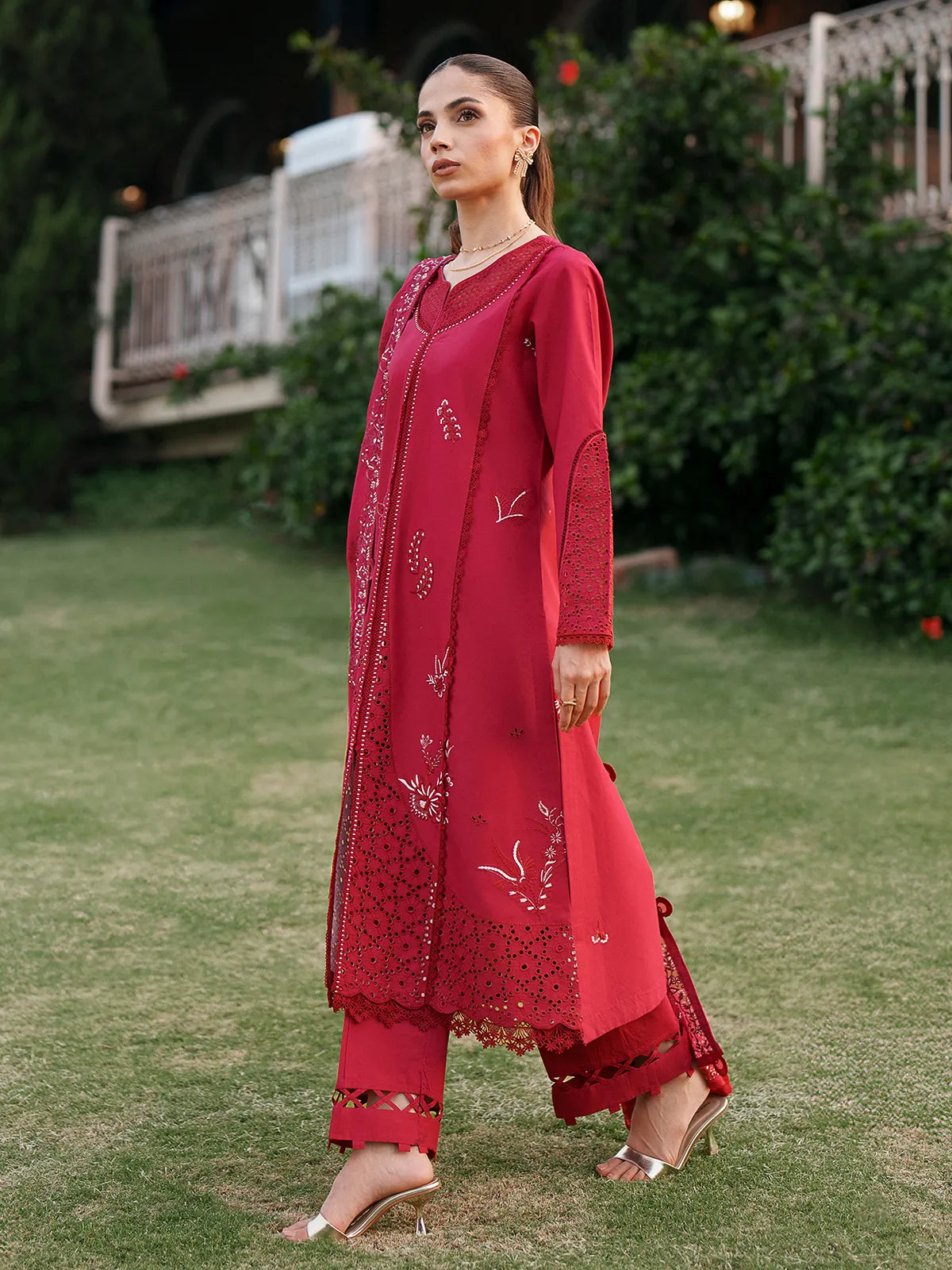 Side full-length view of vibrant red lawn stitched 3-piece suit featuring laser cutwork daman details, embroidered sleeves, and cutwork trouser cuffs from Baad-e-Saba by INEJ.