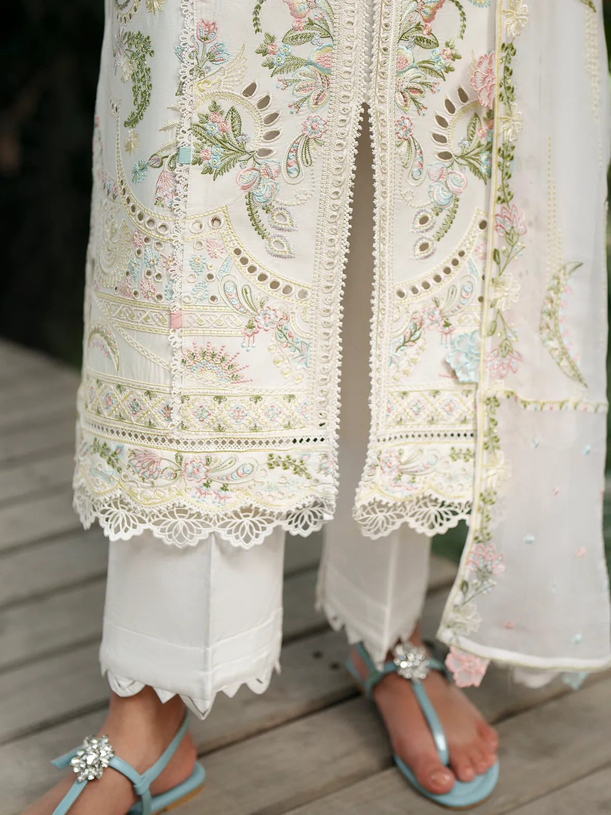 Close-up hem and trouser detail of off-white lawn stitched 3-piece suit featuring pastel floral embroidery, lace-trimmed center slit, scalloped cutwork daman, and cutwork trouser cuffs from Baad-e-Saba by INEJ.