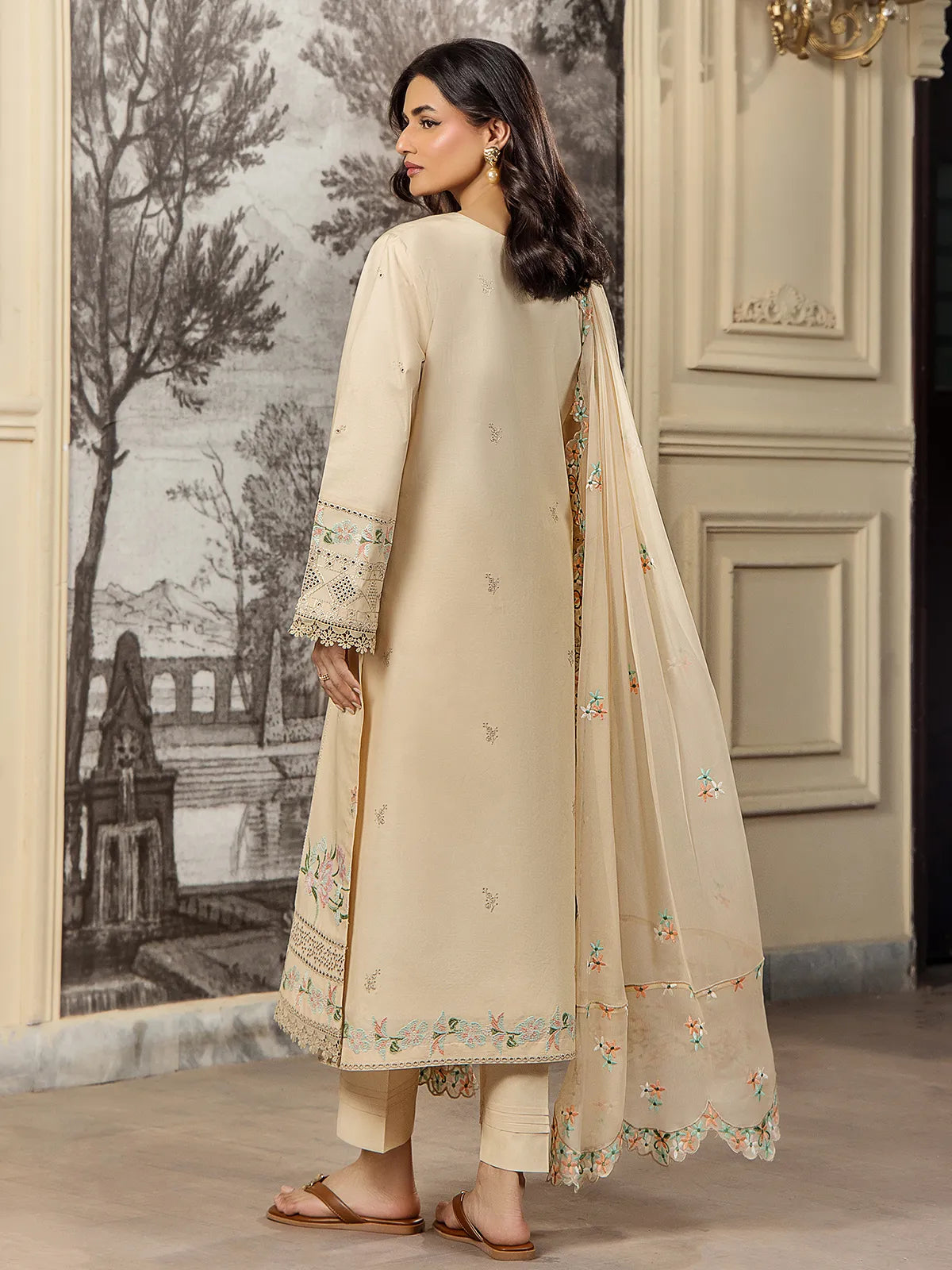 Back view of a model wearing a beige 3-piece embroidered lawn suit showing the flowing scalloped dupatta drape by INEJ.