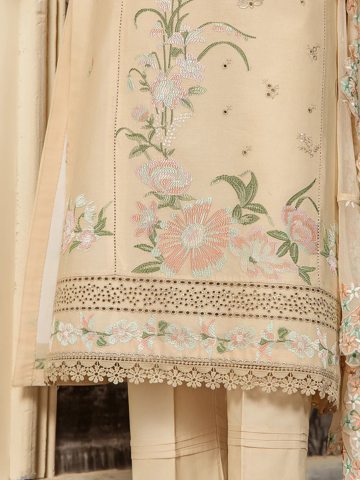 Detailed close-up of pastel floral embroidery, schiffli cutwork border, and lace hem trimming on beige lawn suit by INEJ.