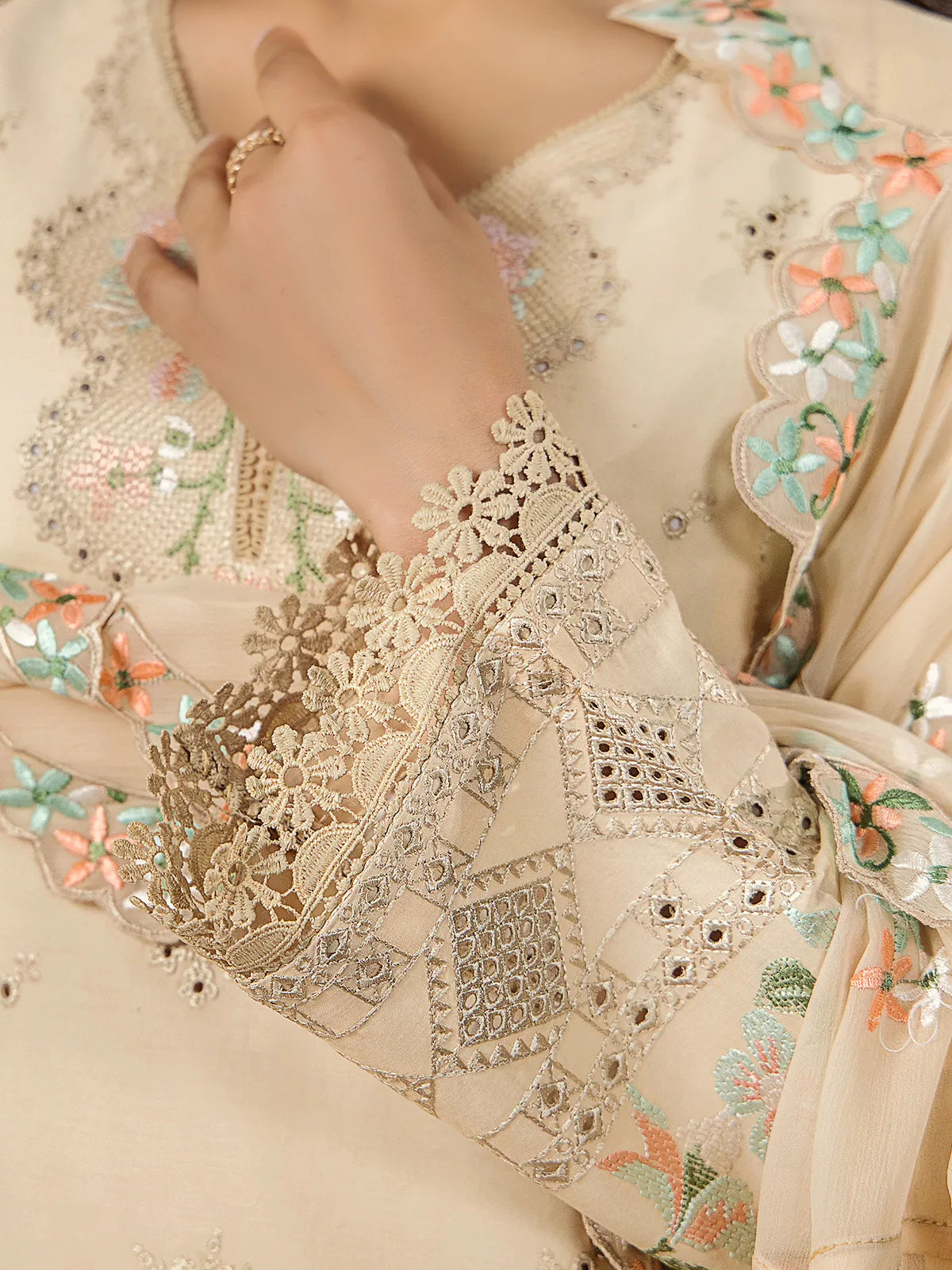 Extreme close-up of geometric schiffli cutwork embroidery and delicate crochet lace edging on beige lawn sleeves by INEJ.