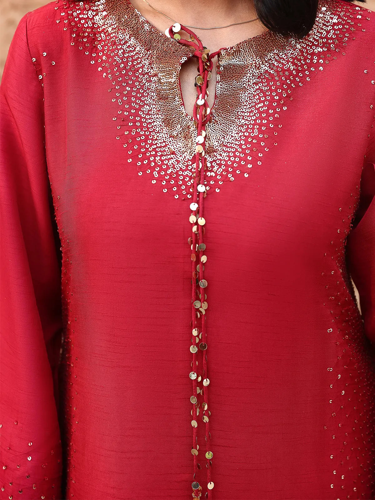 Close-up view of gold sequin embellished neckline with long beaded tassel ties on red silk shirt from Khat by INEJ.