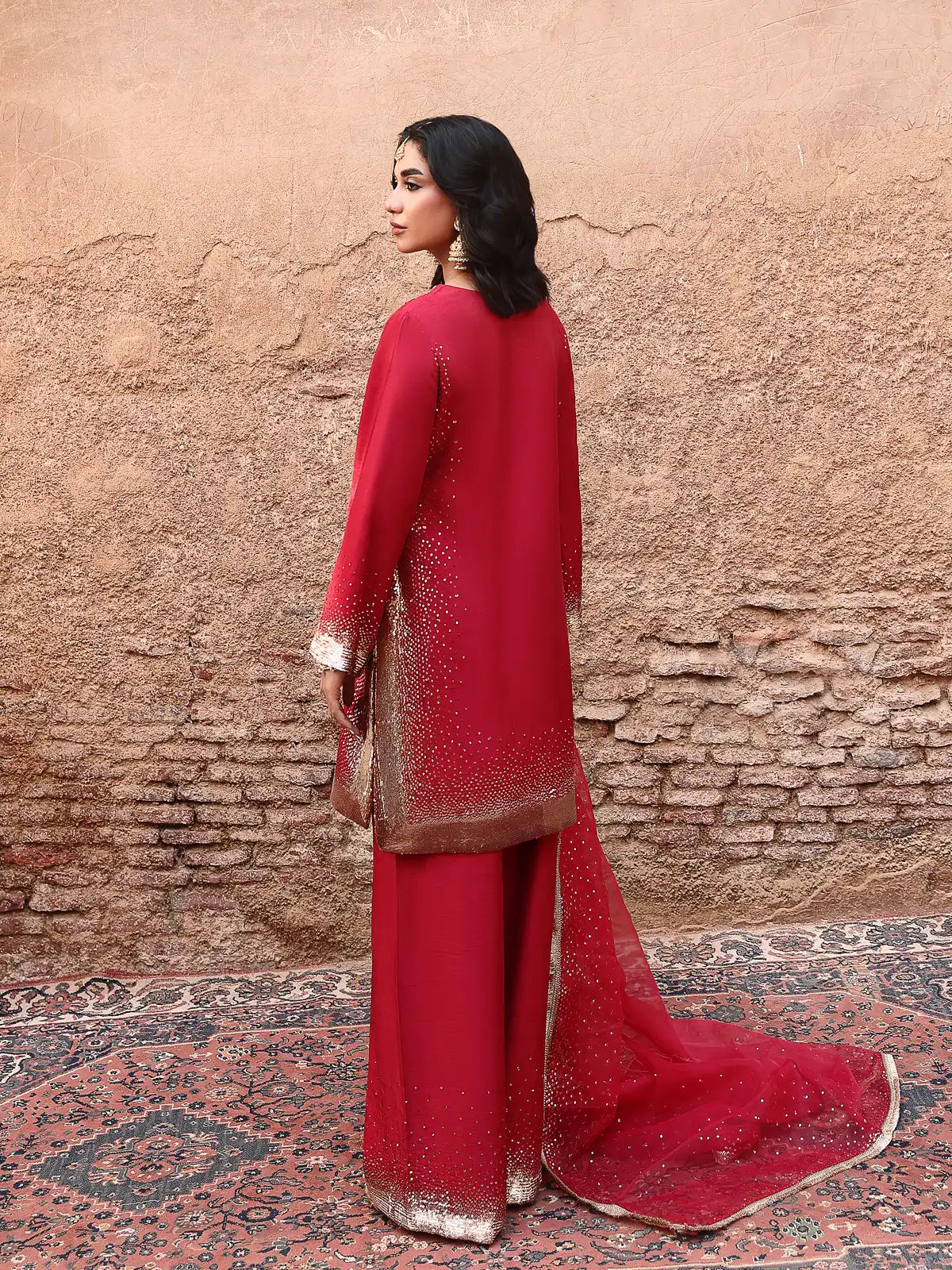 Back view of red stitched 3-piece luxury silk suit with embellished daman and trailing dupatta from Khat by INEJ.
