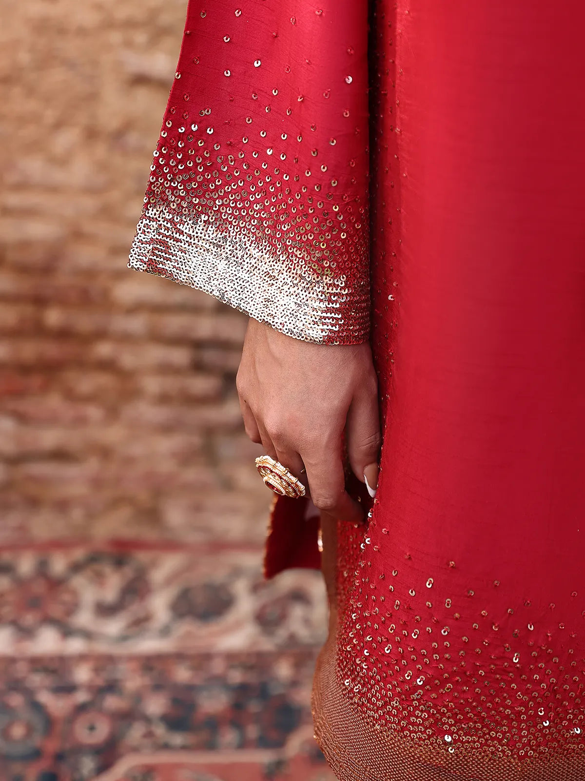 Close-up view of sequin embellishments on red shirt sleeve cuff and curved daman from Khat by INEJ.