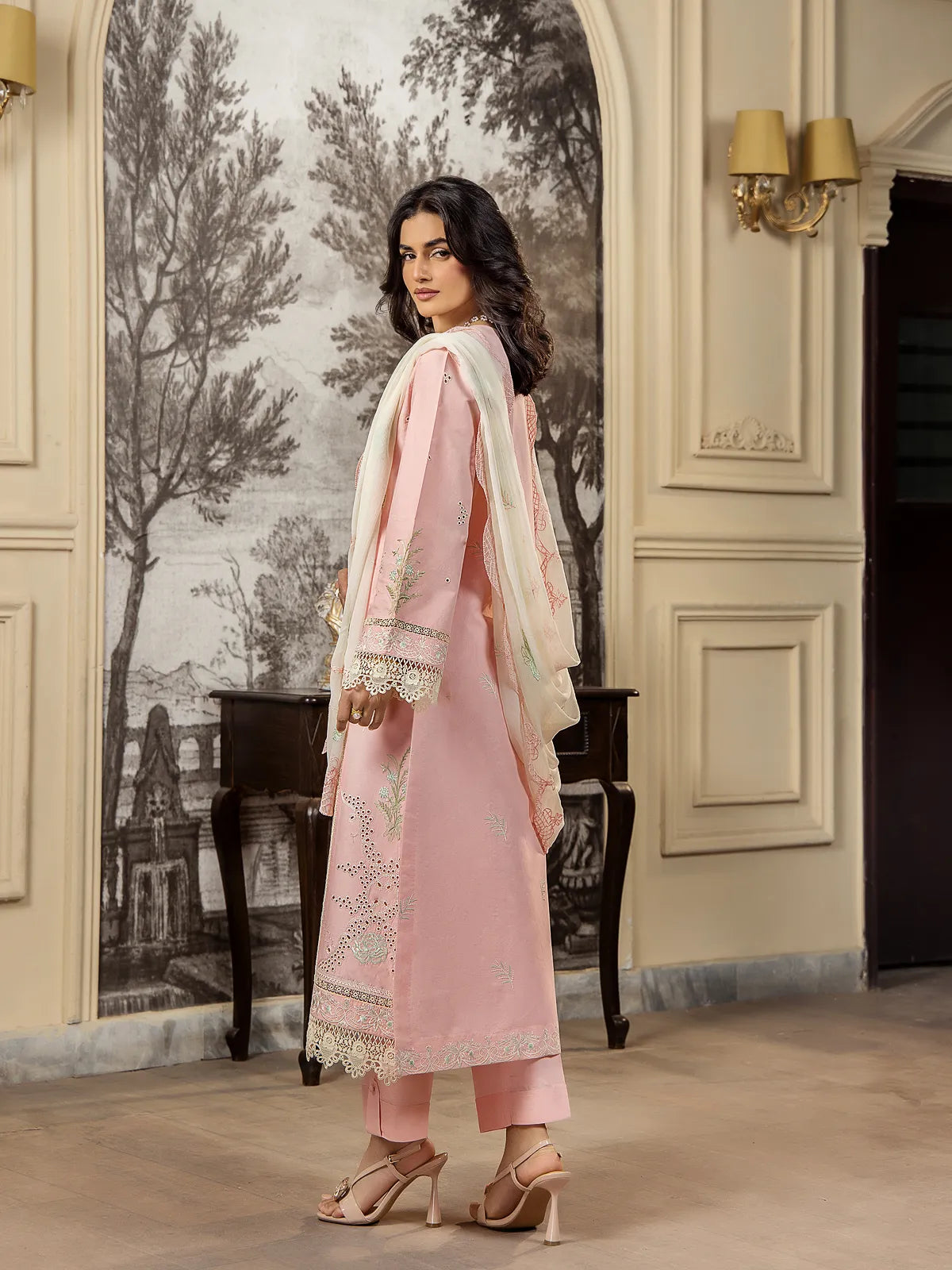 Side view of a model wearing a soft pink 3-piece embroidered lawn suit displaying the draped off-white dupatta and side panel finish by INEJ.